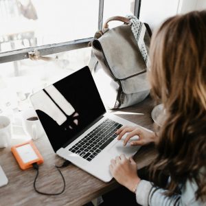 A young woman works remotely at a café, using her laptop and external hard drive.